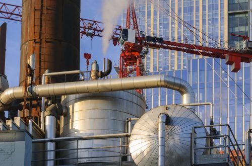 An industrial powerplant, large metal containers, steam being generated and rising, pipework.